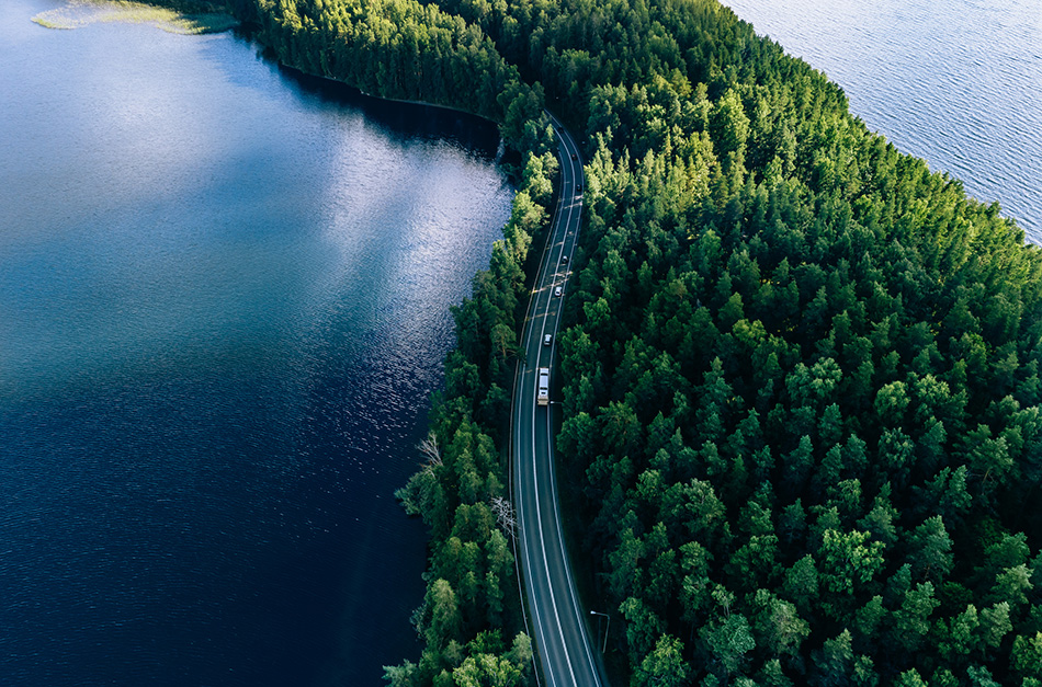 Vehicles driving down a road surrounded by a body of water and trees.