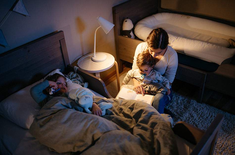 A woman reading book to her children with a lamp on.